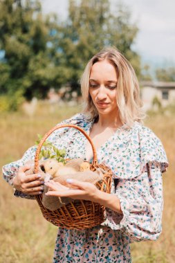 Genç bir kadın bir sepet ördek yavrusu tutuyor ve gülümsüyor.