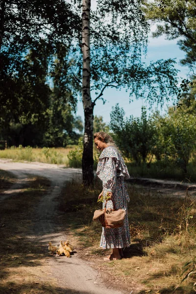 Kırsal kesimden genç bir kadın küçük ördekleri beslemek için eğildi.