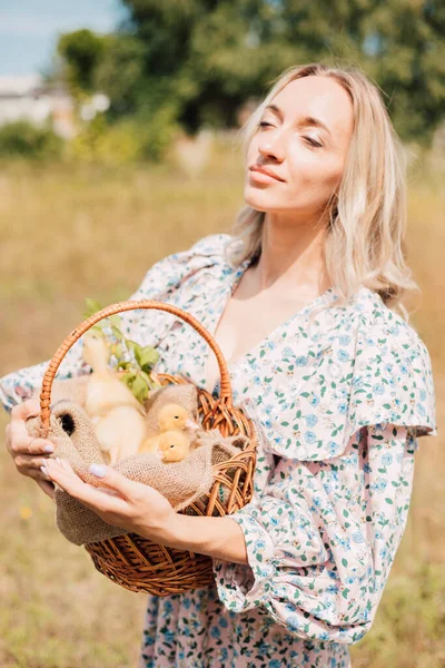 Bir kadın elinde ördek yavrusuyla bir sepet tutuyor ve gözlerini kapıyor.