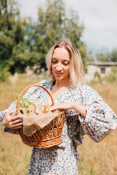 Genç bir kadın bir sepet ördek yavrusu tutuyor ve gülümsüyor.