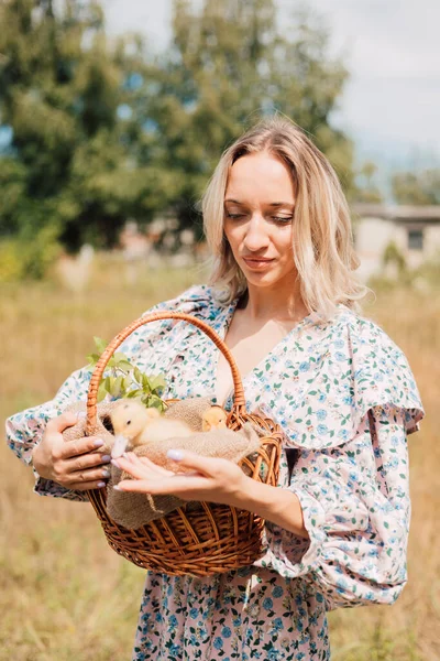 Genç bir kadın bir sepet ördek yavrusu tutuyor ve gülümsüyor.