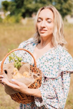 Bir kadın elinde ördek yavrusuyla bir sepet tutuyor ve gözlerini kapıyor.