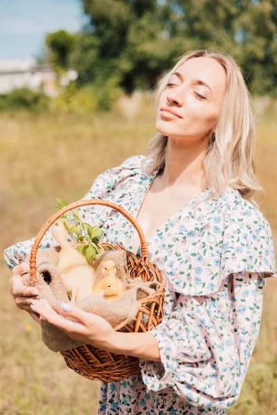 Bir kadın elinde ördek yavrusuyla bir sepet tutuyor ve gözlerini kapıyor.