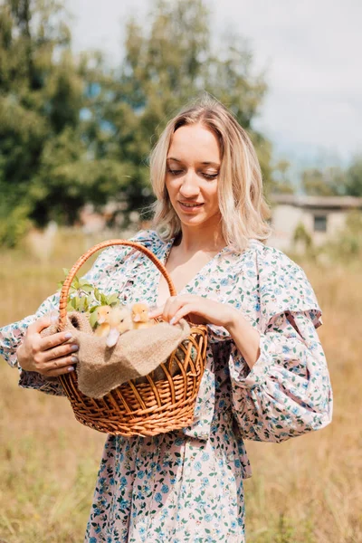 Genç bir kadın bir sepet ördek yavrusu tutuyor ve gülümsüyor.