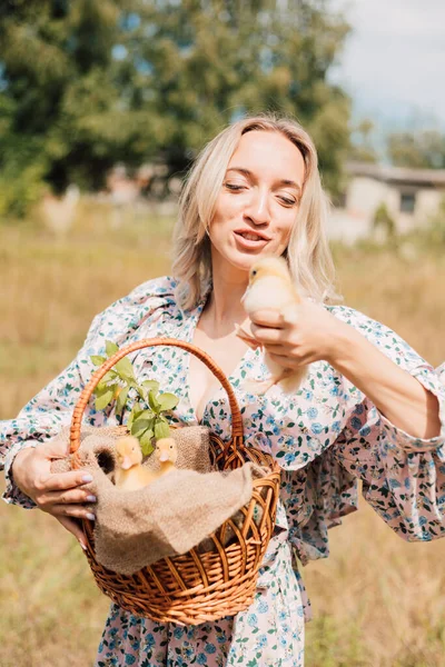 Bir kadın bir elinde ördek yavrusu, diğer elinde ördek yavrusu olan bir sepet tutar.