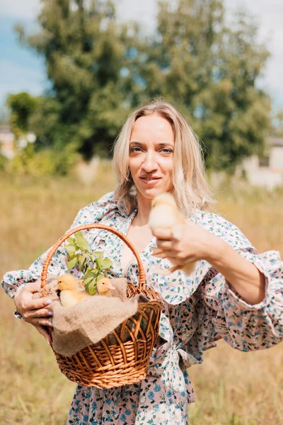 Bir kadın bir elinde ördek yavrusu, diğer elinde ördek yavrusu olan bir sepet tutar.