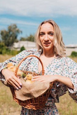 Kırsal kesimde genç bir kız elinde ördek yavrusu dolu bir sepet tutuyor.