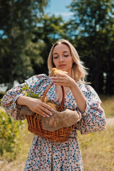 Bir kadın bir sepet tutuyor ve bir elinde küçük bir ördek yavrusu tutuyor.