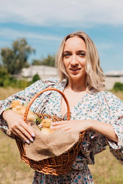 Kırsal kesimde genç bir kız elinde ördek yavrusu dolu bir sepet tutuyor.