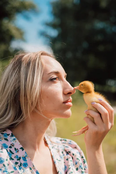 A young woman holds a small duckling in her hand touching its beak with her nose — Fotografia de Stock