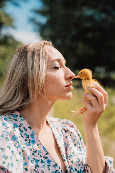 Eine junge Frau hält ein kleines Entlein in der Hand, das seinen Schnabel mit der Nase berührt — Stockfoto