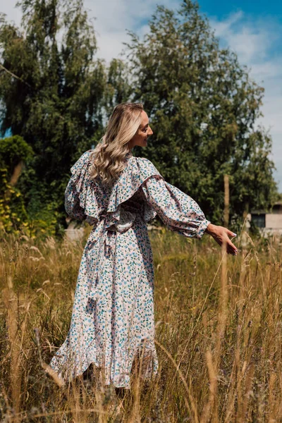 Uzun elbiseli genç bir kız tarlada yürüyor.