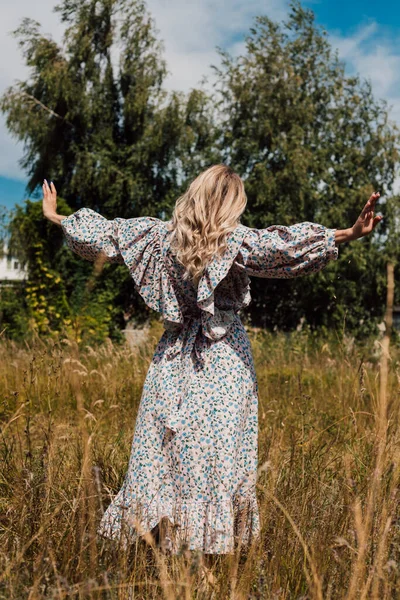 Uzun elbiseli genç bir kız tarlada yürüyor.