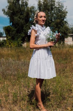 Kırsal elbiseli genç bir kız elinde çiçekleri tutuyor.
