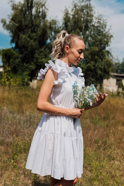 Une jeune fille en robe rustique tient des fleurs dans ses mains — Photo