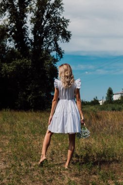 Kırsal elbiseli bir kız arkasını döndü ve elinde çiçekler tuttu.