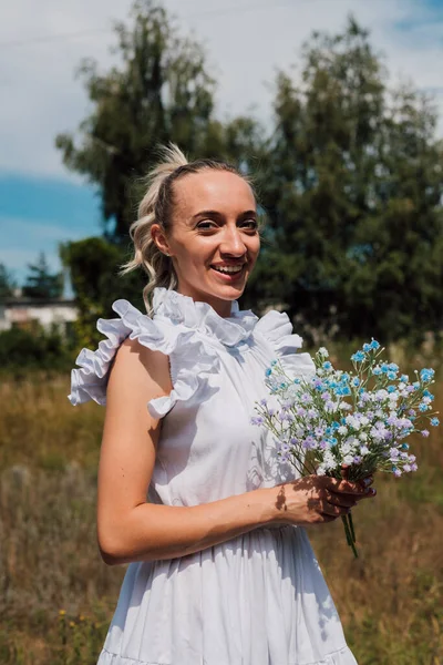 Een jong mooi meisje houdt bloemen in haar handen en glimlacht — Stockfoto