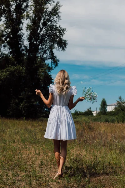 A girl in a rustic dress turned her back and holds flowers in her hand — Photo
