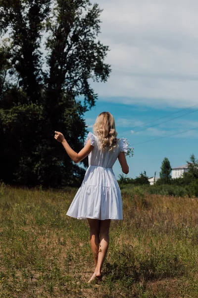 A girl in a rustic dress turned her back and holds flowers in her hand —  Fotos de Stock