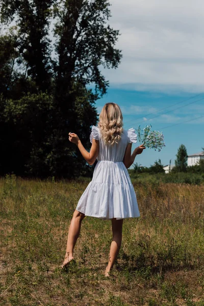 A girl in a rustic dress turned her back and holds flowers in her hand — Fotografia de Stock