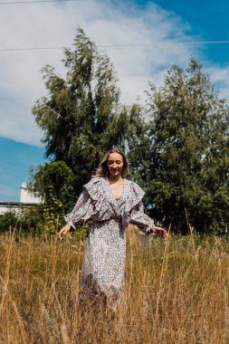 Uzun elbiseli genç bir kız tarlada yürüyor.