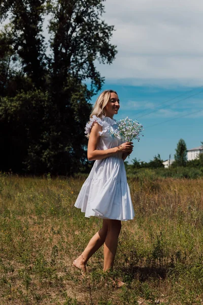 A girl walks through a field in the countryside with flowers in her hands — Photo