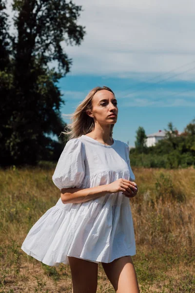 Mladá žena stojí na poli a dívá se do dálky — Stock fotografie