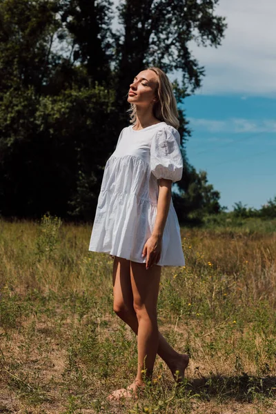 A young beautiful woman in a short dress stands closing her eyes dreams — Stock Photo, Image