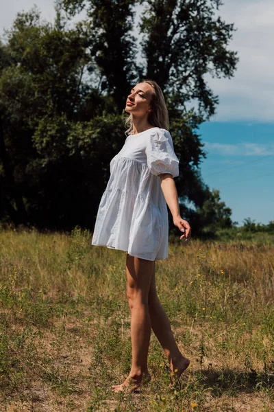 A young girl in a short dress stands in nature with her arms spread — 스톡 사진