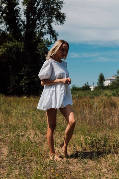 Genç bir kadın çıplak ayakla tarlada dikiliyor ve aşağıya bakıyor.