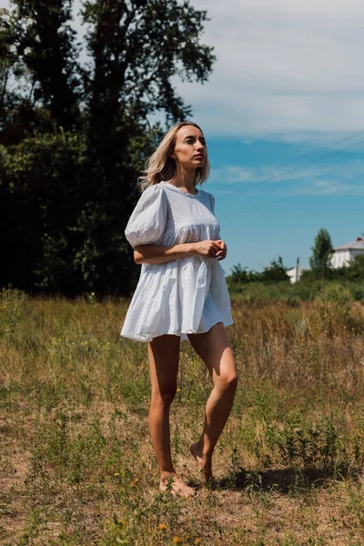 En ung kvinna står barfota i ett fält och tittar in i fjärran — Stockfoto