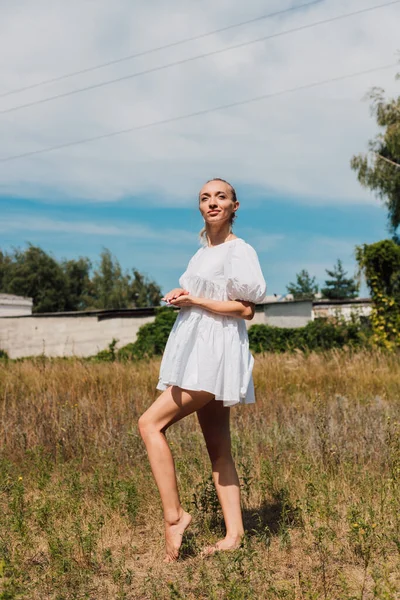 Une jeune femme se tient dans un champ et regarde au loin — Photo