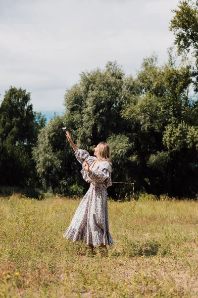 A woman with bare feet in a long rustic dress stretches her hands to the sky — Photo