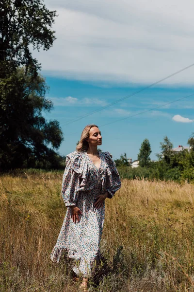 A young woman in a rustic dress stands in a field and looks up — Photo
