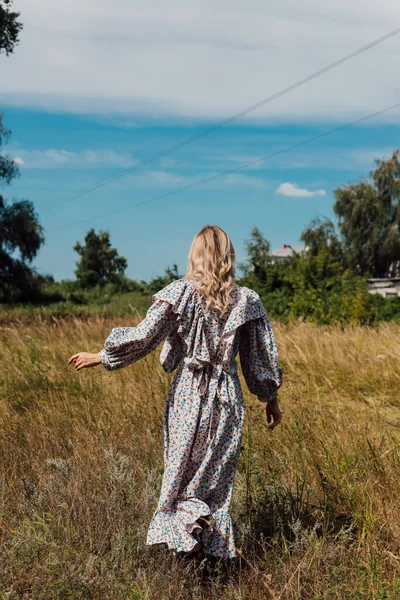 A young woman in a long country dress stands in a field with her back forward — Photo