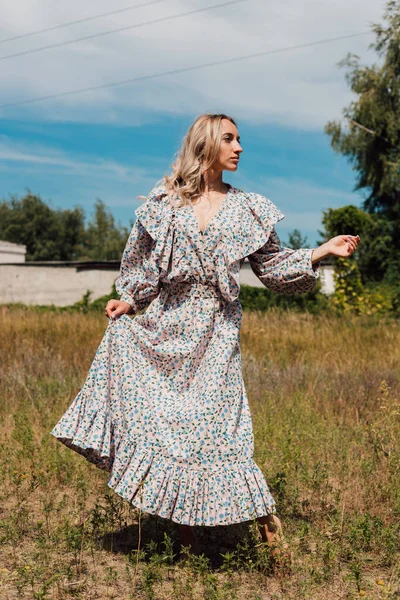 A young woman with bare feet in a long country dress dances in a field — Photo