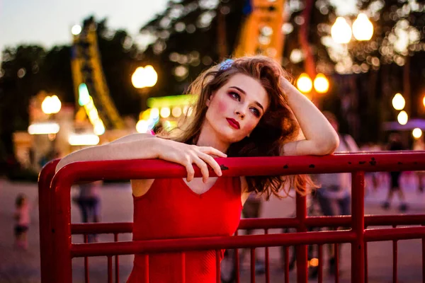 Kırmızı elbiseli güzel bir kız akşam vakti parkta kırmızı bir çerçeveye yaslanır.