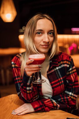 A young beautiful blonde holds a glass with a cocktail in a restaurant clipart