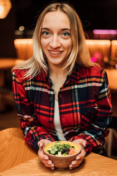Молода жінка сидить в ресторані, обіймаючи тарілку руками і посміхаючись — стокове фото