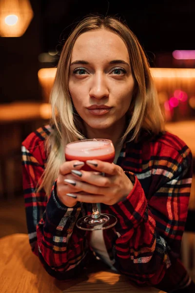 Eine junge schöne Blondine hält in einem Restaurant ein Glas mit einem Cocktail in der Hand — Stockfoto