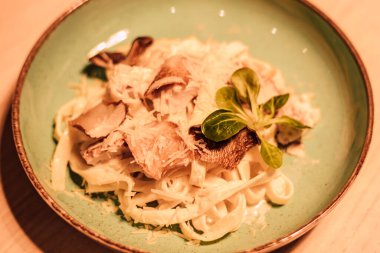 Yeşil seramik tabakta peynirli, etli ve otlu makarna.