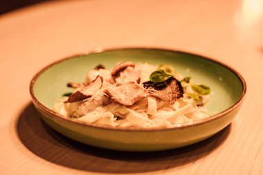 Yeşil seramik tabakta peynirli, etli ve otlu makarna.