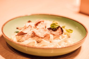 Yeşil seramik tabakta peynirli, etli ve otlu makarna.