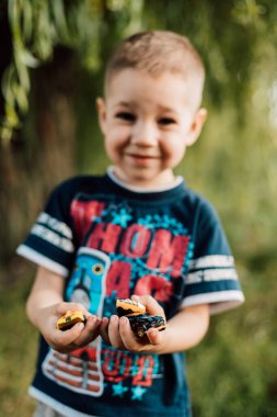 Küçük bir çocuk oyuncakları elinde tutuyor ve doğada bir ağacın altında gülümsüyor.