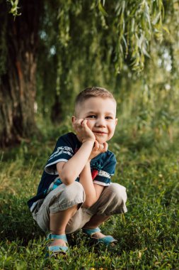 Küçük bir çocuk bir ağacın altına çömelmiş, eli başını destekliyor ve kızgın.