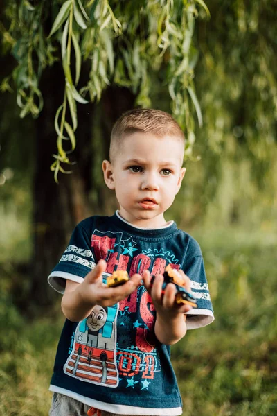 A little boy holds a toy in his hands and plays in nature under a tree — Foto Stock