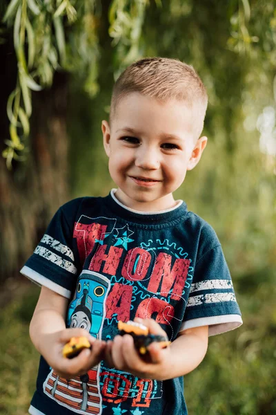 A small child holds toys in his hands and smiles in nature under a tree — Foto Stock