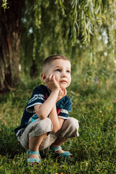 A little boy crouched under a tree, his hand propping up his head and angry — Foto Stock