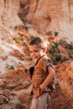 Küçük bir çocuk kumun ortasında duruyor ve elinde bir oyuncak tutuyor.