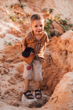 Küçük bir çocuk kumun ortasında duruyor ve elinde bir oyuncak tutuyor.